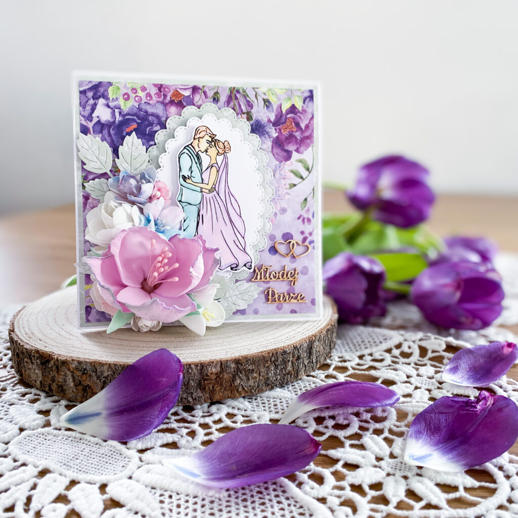 ręcznie wykonana kartka ślubna w fioletowej kolorystyce. Na kartce znajduje się bardzo rozbudowana kompozycja kwiatowa. Całość zapakowana jest w ozdobne pudełko.