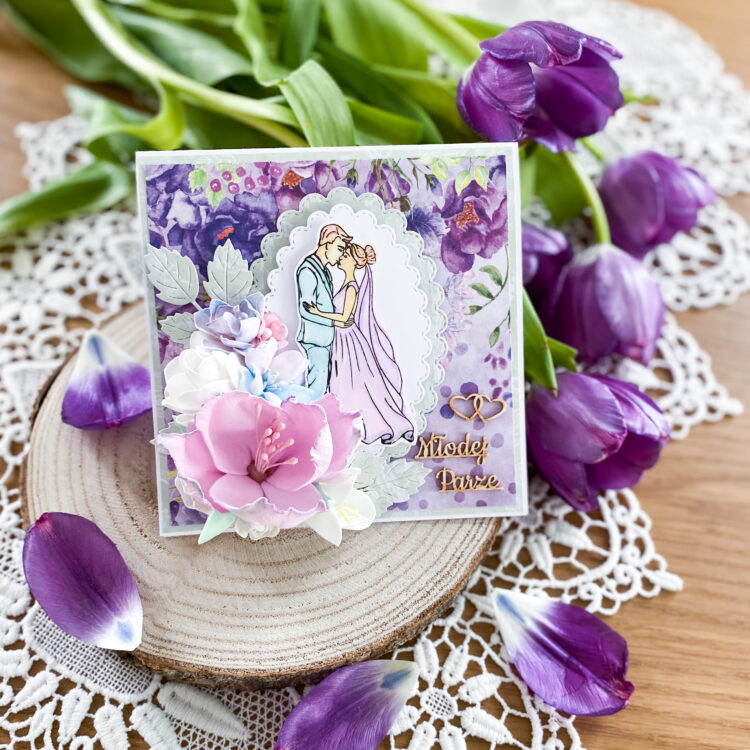 ręcznie wykonana kartka ślubna w fioletowej kolorystyce. Na kartce znajduje się bardzo rozbudowana kompozycja kwiatowa. Całość zapakowana jest w ozdobne pudełko.