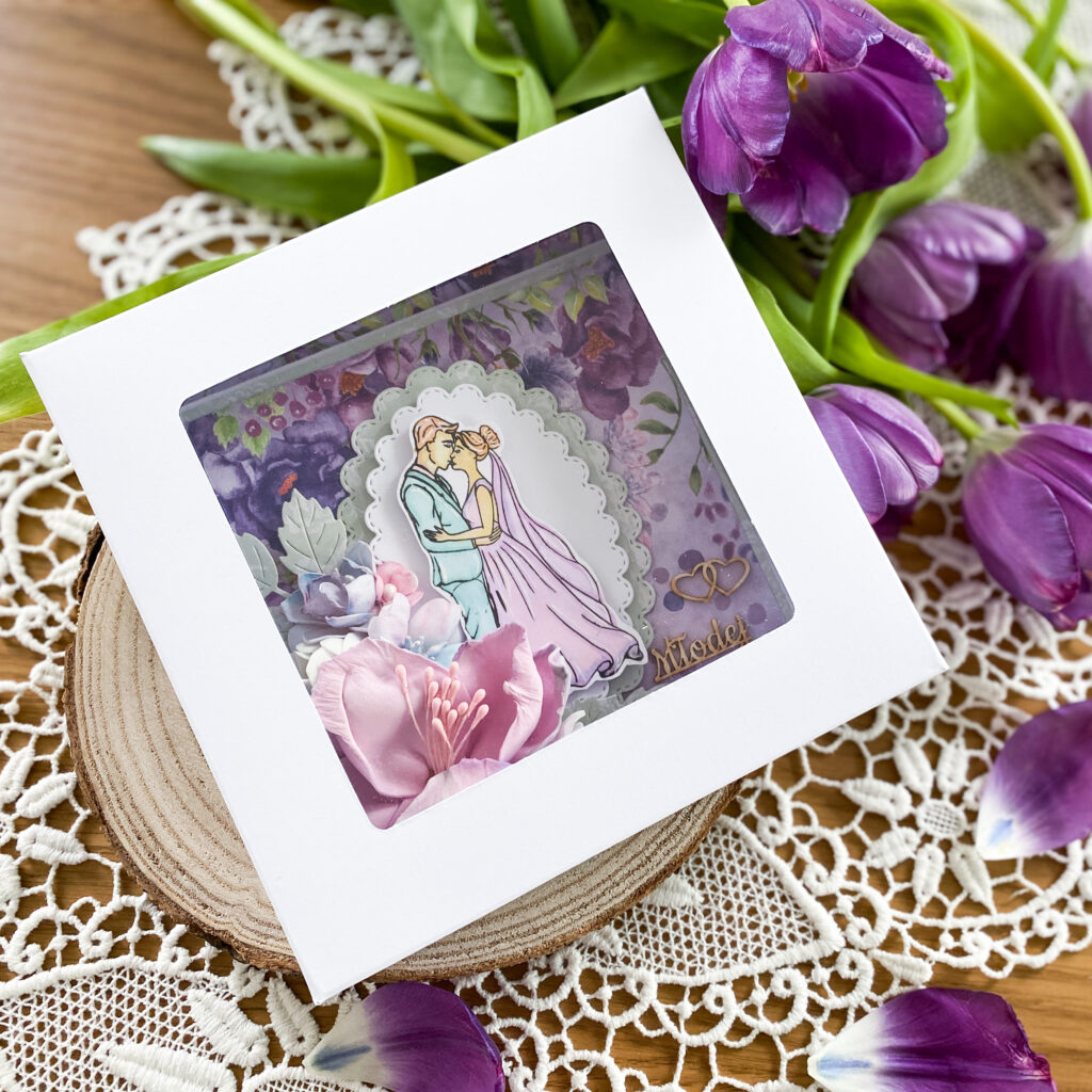 ręcznie wykonana kartka ślubna w fioletowej kolorystyce. Na kartce znajduje się bardzo rozbudowana kompozycja kwiatowa. Całość zapakowana jest w ozdobne pudełko.